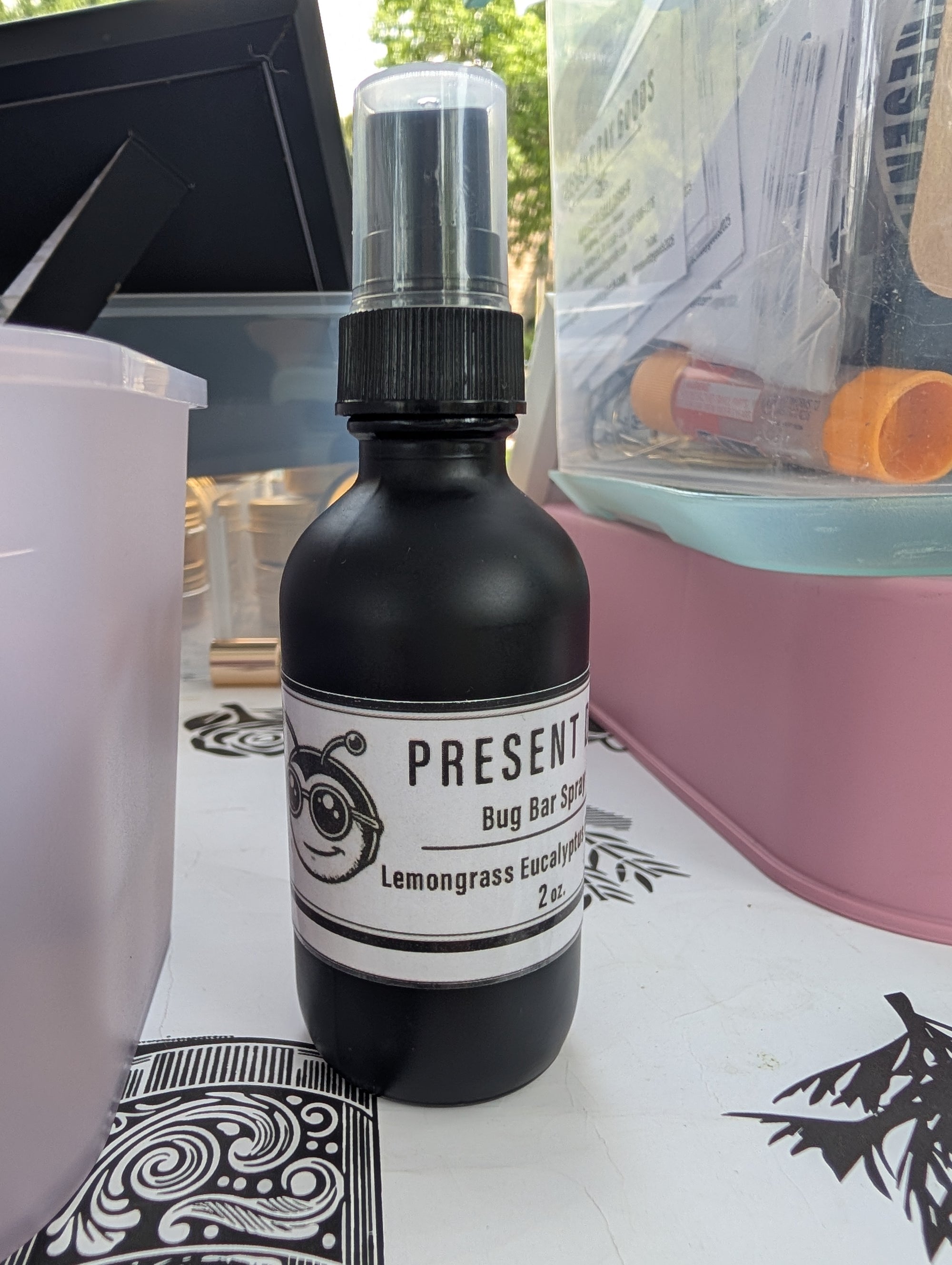 Black bottle of 'Present' bug bar spray on a table with a blurred background