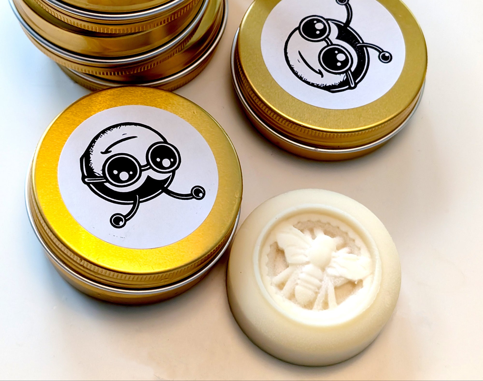 Gold tins with white labels featuring a bee design, stacked on a light background.
