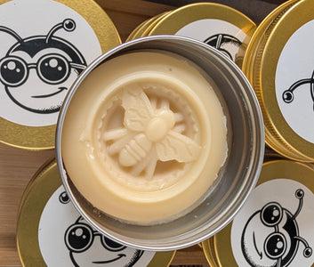 Beeswax product with a bee design on top, surrounded by containers with a bee logo.