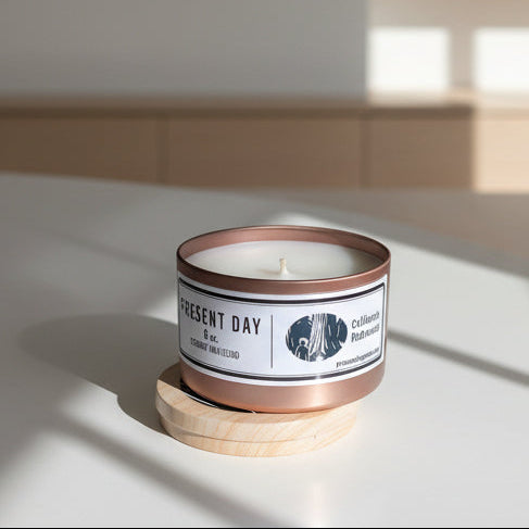 Candle in a metal container with a wooden print base on a white surface