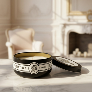 Candle in a black container with 'Present Day' branding on a marble surface.