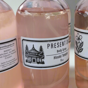 Bottle of Present Day Body Spray with a black cap on a white background