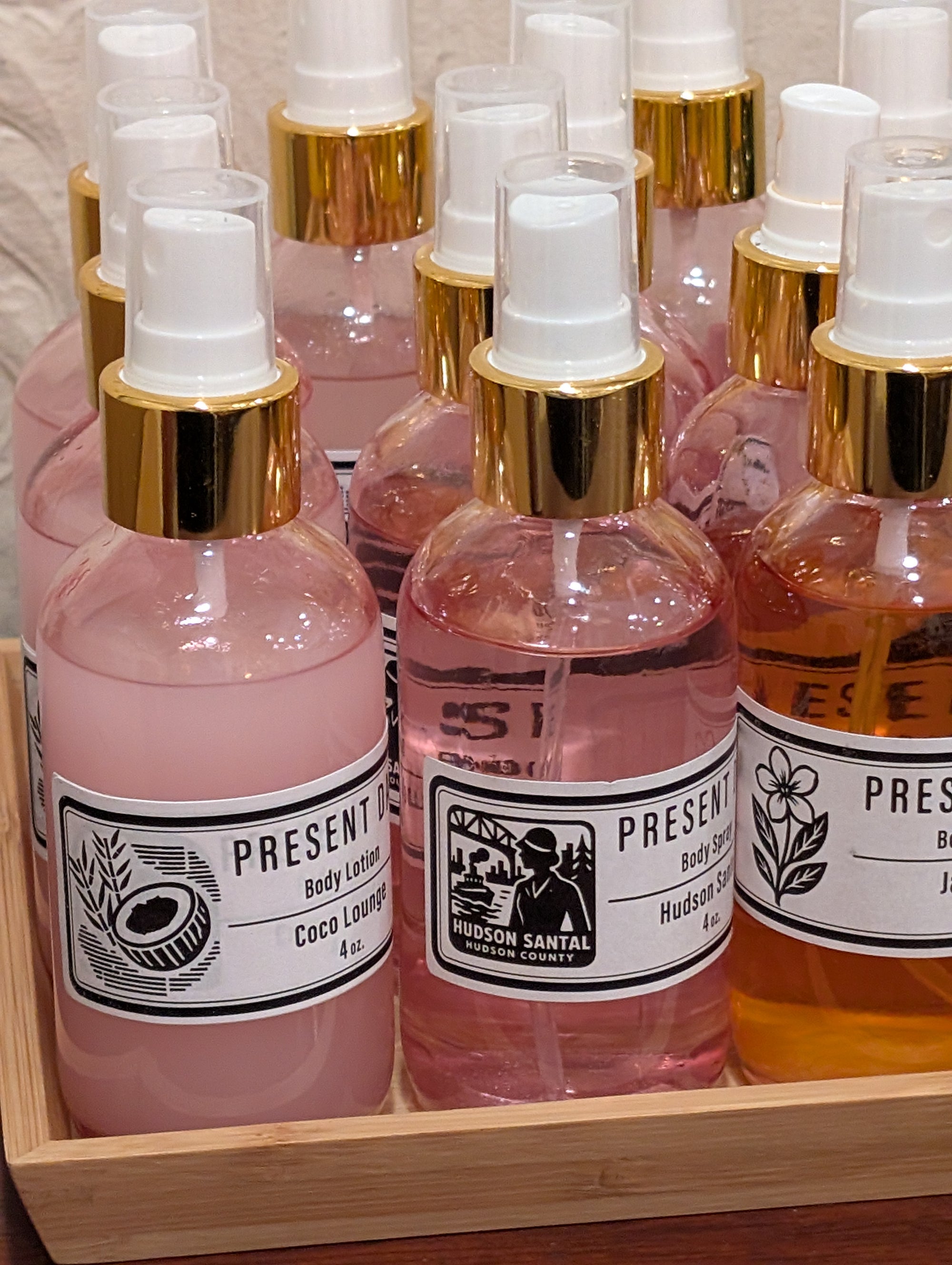 Bottles of Hudson Santal body spray in pink and orange with gold caps on a wooden tray.