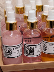 Bottles of Hudson Santal body spray in pink and orange with gold caps on a wooden tray.
