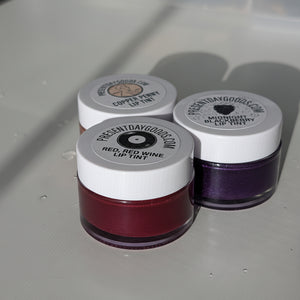Three small jars with lip tint on a reflective surface