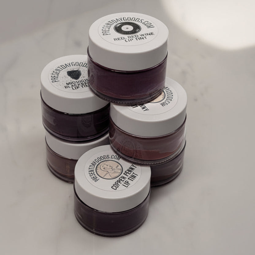 Four jars of lip tint from Present Day Goods on a marble surface