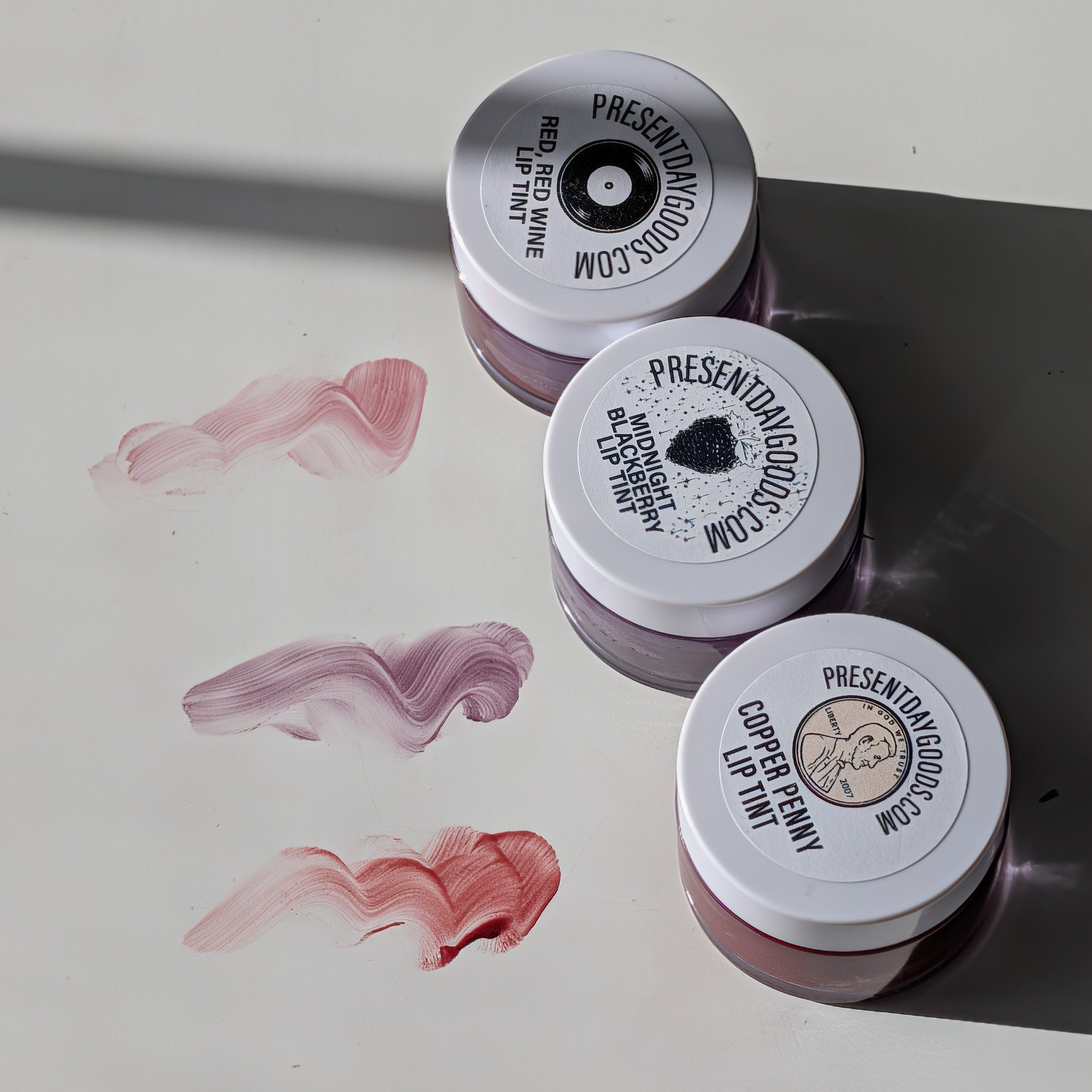 Three small containers with white lids on a light surface with paint swatches.