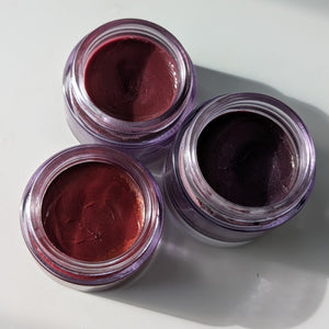 Three small jars of dark red cream on a white background