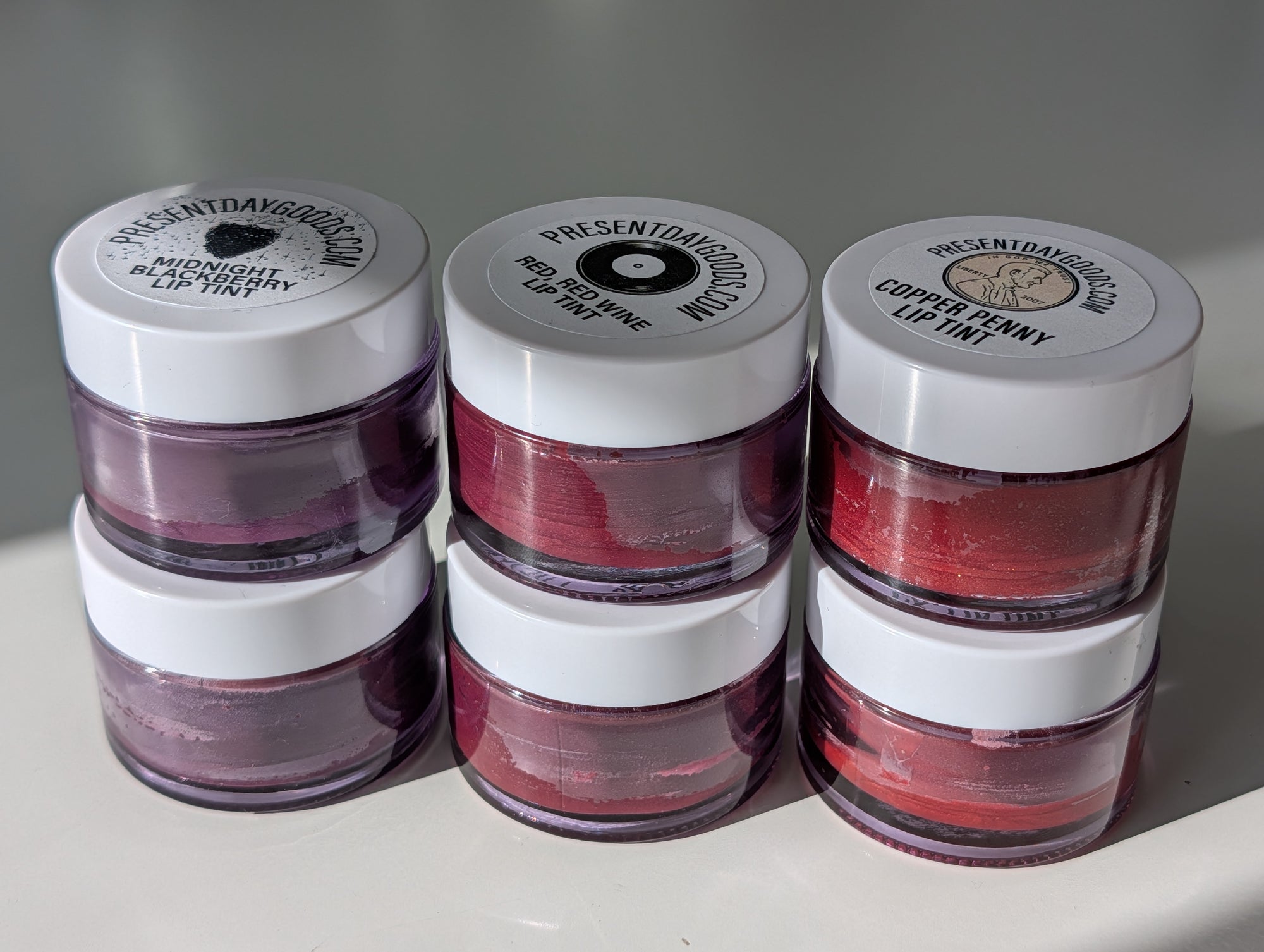 Three lip balm containers with visible labels on a white surface.