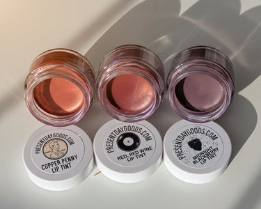 Three lip tint containers with visible colors and 'Present Day Goods' branding on a light background.