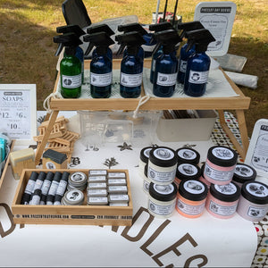 Outdoor market stall with various products including bottles and containers on a table.