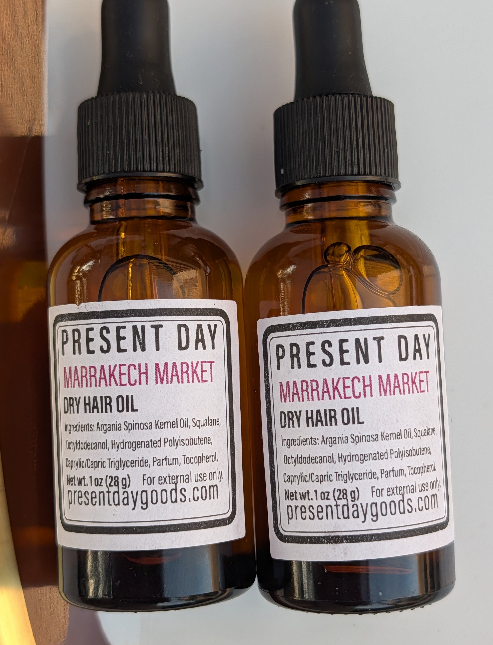 Two amber glass dropper bottles of Present Day Marrakech Market Dry Hair Oil arranged vertically on a white background.