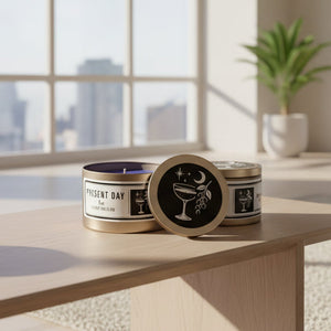 Two candles in tins with black labels and golden lids featuring graphics on a white surface