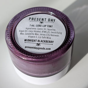 Lip tint container with purple lid and white base on a light background