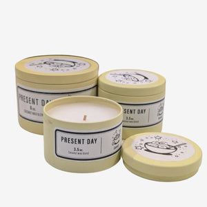 Three 'Present Day' candles in yellow tins on a white background