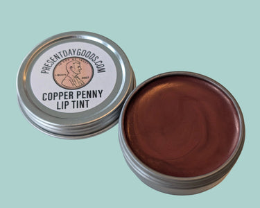 Copper penny lip tint in a metal container with 'PresentDayGoods.com' label on a light background