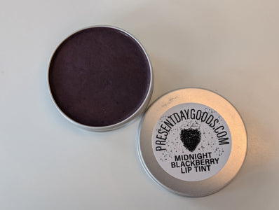 Tin of Midnight Blackberry lip tint with 'Present Day Goods' label on a light gray background