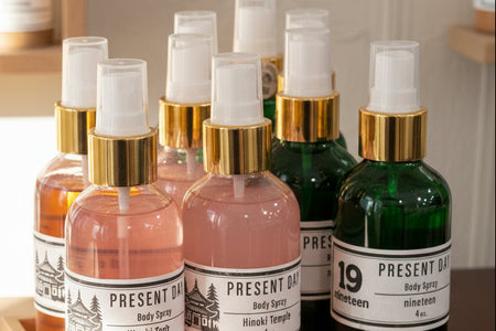 Collection of Present Day body spray bottles on a wooden tray with a neutral background.