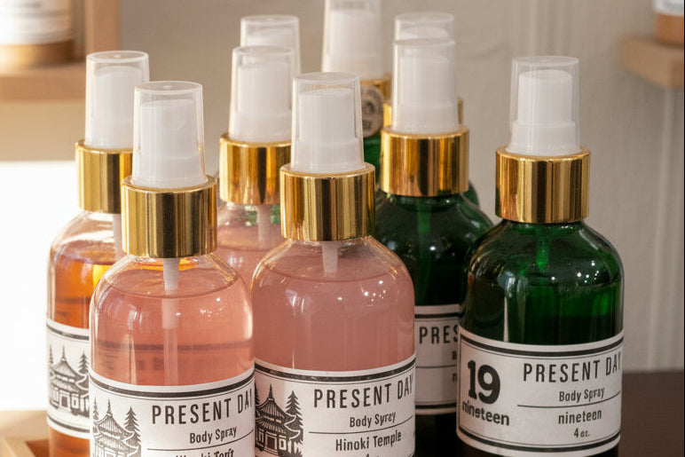 Collection of Present Day body spray bottles on a wooden tray with a neutral background.