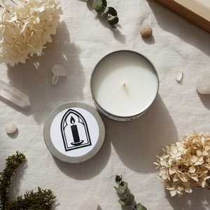 Candle in a tin with a lid featuring a candle design, surrounded by flowers and crystals on a textured surface.