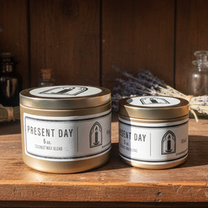 Two 'Present Day' candles on a surface with a blurred background