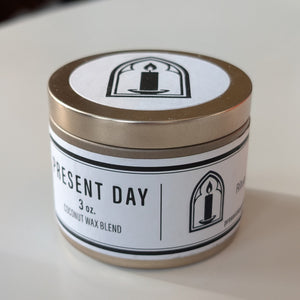 Candle jar with 'Present Day' label on a white surface
