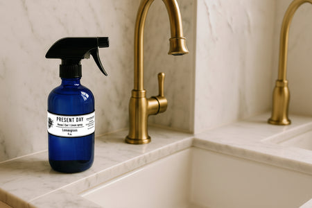 BLue spray bottle with black nozzle on a marble countertop next to a gold faucet.