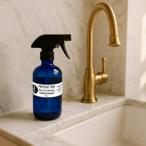 Blue spray bottle with black nozzle on a marble countertop next to a gold faucet.