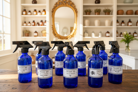 Blue spray bottles with black nozzles on a wooden surface, with a decorative mirror and shelves in the background.