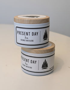 Two 'Present Day' candles stacked on a light surface