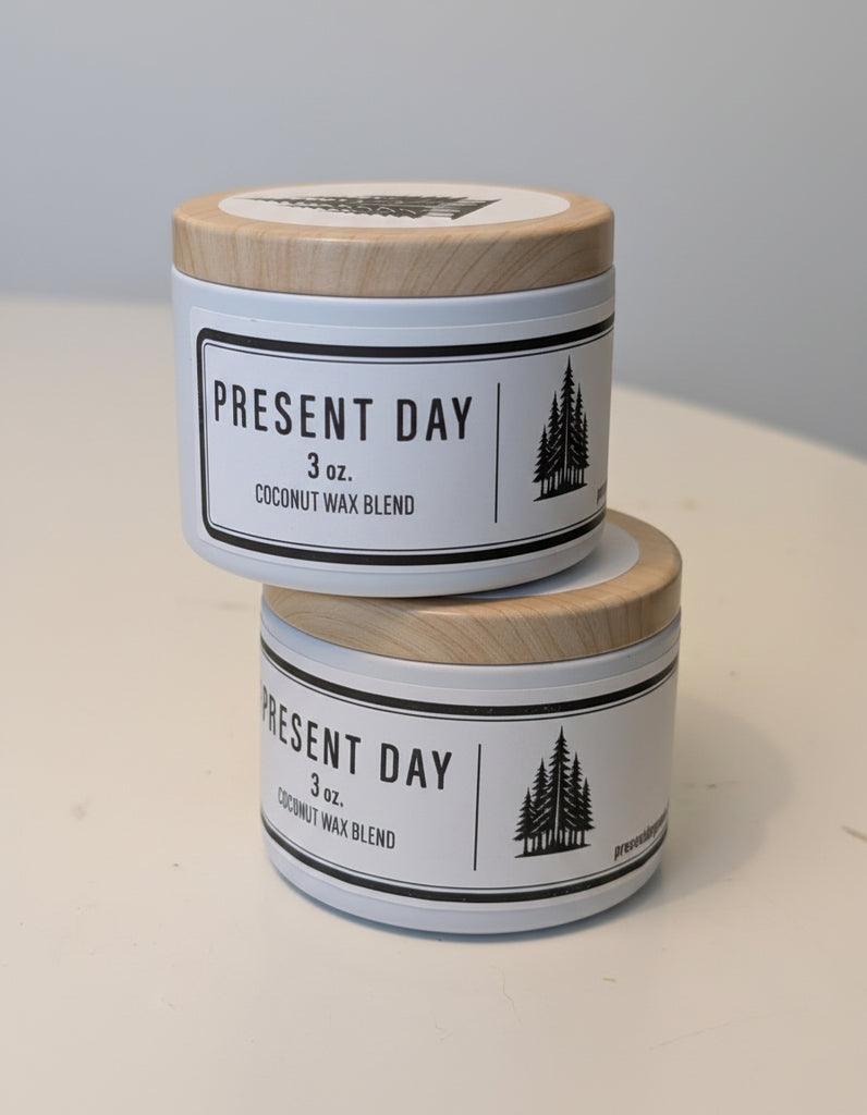 Two 'Present Day' candles stacked on a light surface