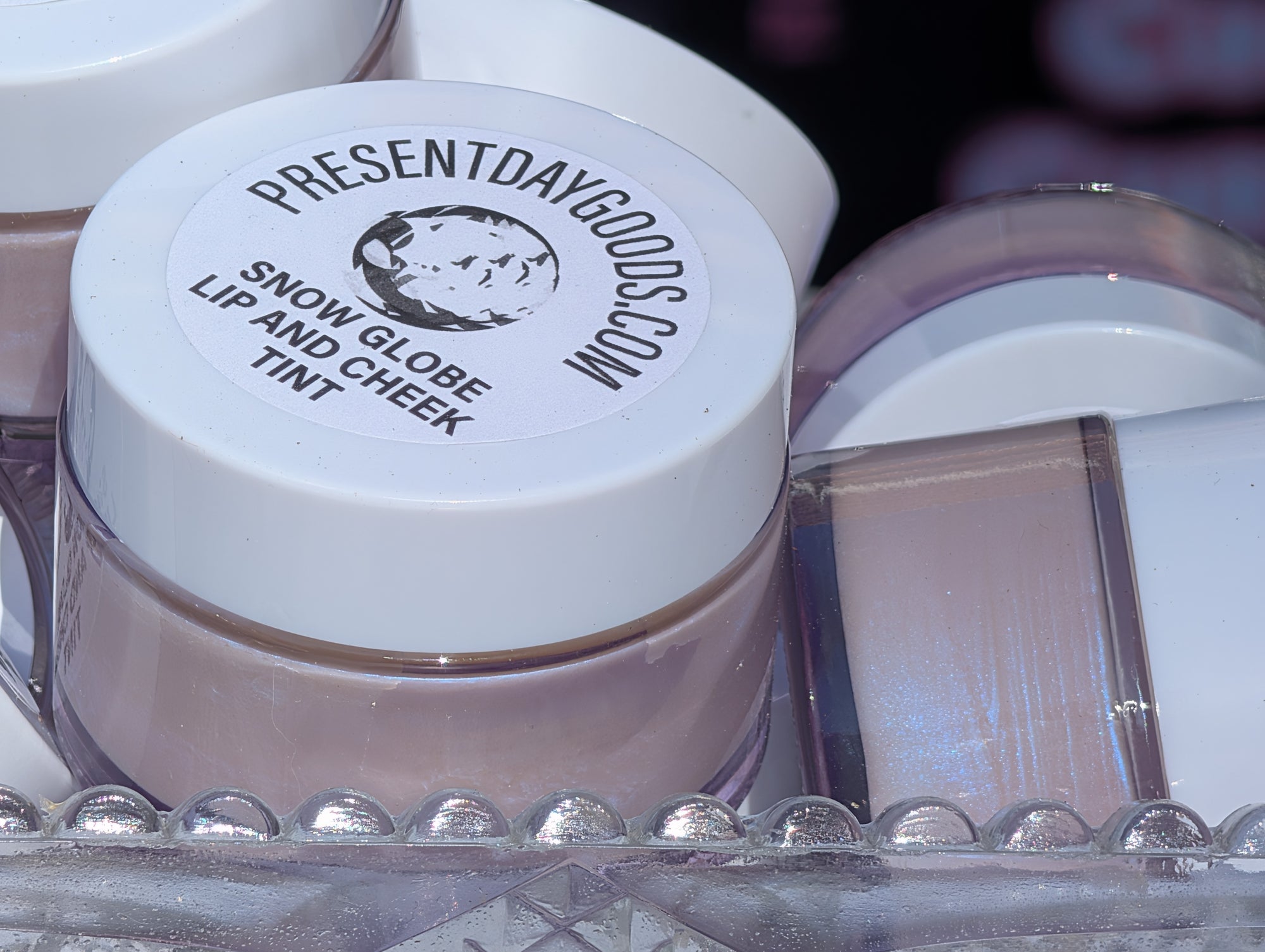 Snow globe lip and cheek tint jar with visible brand name on a clear stand.