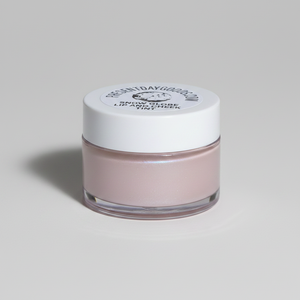 A small clear jar of lip gloss with a white lid, filled with a pale pink shimmering gloss, on a light gray background.