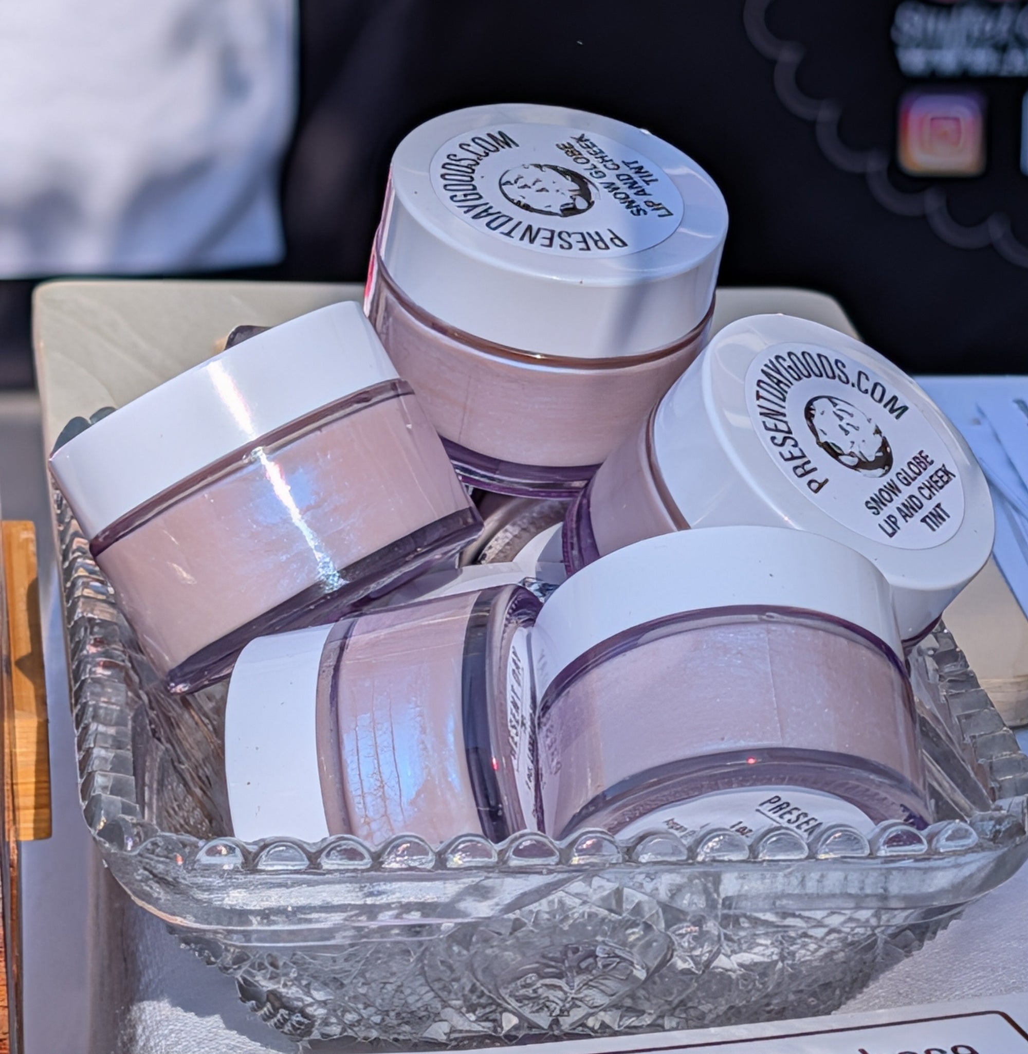 Three pink jars with white lids in a clear plastic container on a table.