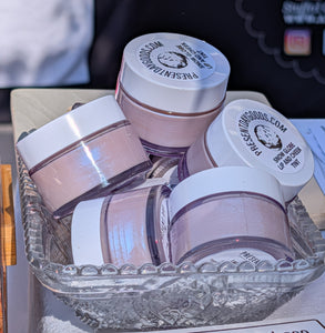 Three pink jars with white lids in a clear plastic container on a table.