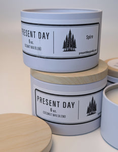 Two 'Present Day' coconut wax blend container candles with wooden lids on a light surface.