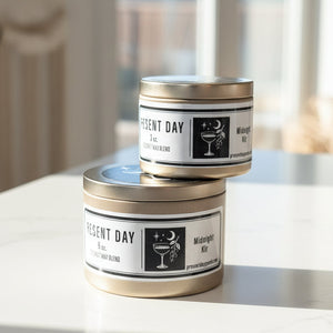 Two tins of 'Present Day' Midnight Kir candle blend on a white surface.