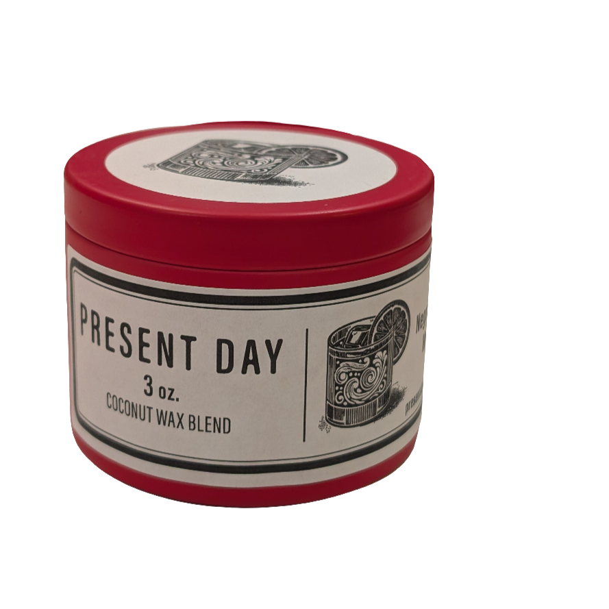 A red tin candle with a label that reads 'PRESENT DAY 3 oz. COCONUT WAX BLEND'.