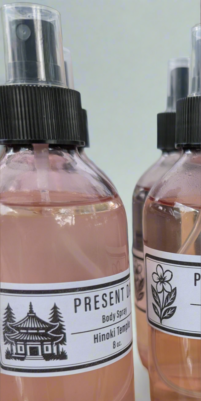 Two bottles of Present Day Goods body spray with labels on a light background