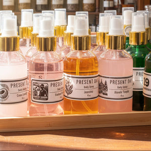Set of body spray bottles with different colored bottles on a wooden tray against a textured wall.