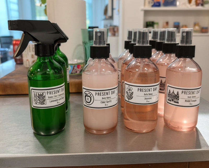Set of bottles with black sprayer nozzles and labels on a metallic surface.