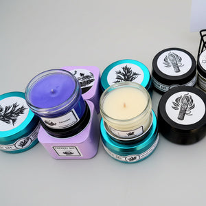 Collection of various candles with different colored containers and labels on a white background.