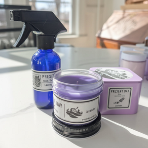 Blue spray bottle and lavender candle with 'Present Day' branding on a light surface.