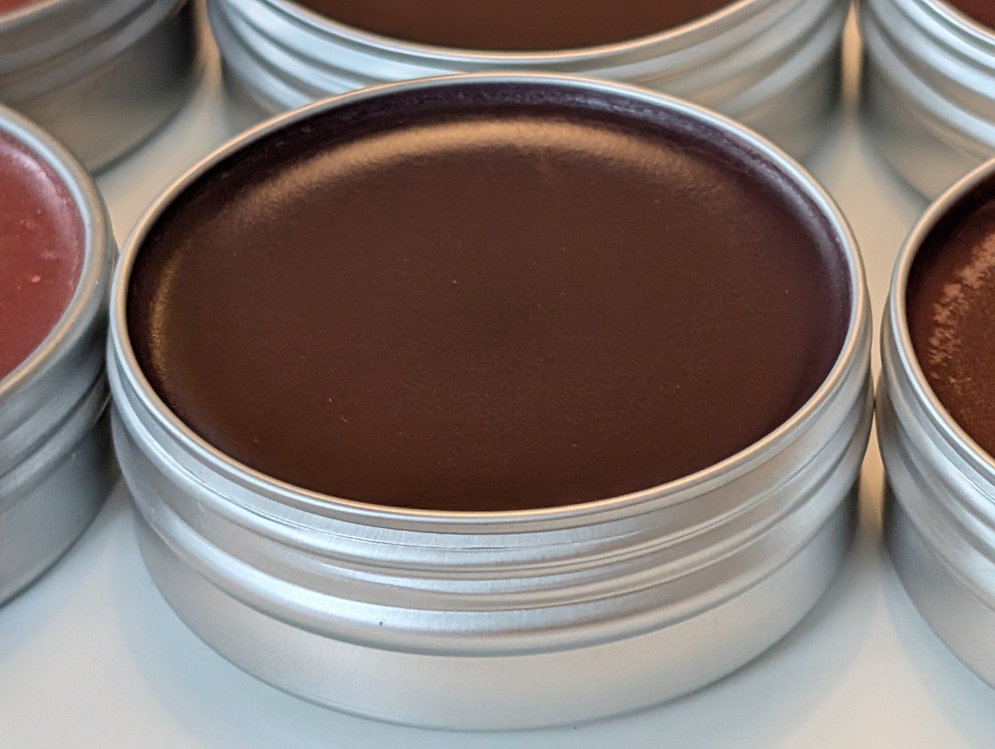 Metal tins with midnight blackberry lip tint contents on a white surface