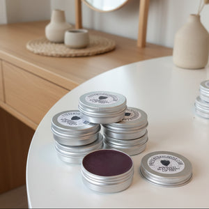Stack of metal tins with midnight blackberry lip tint contents on a white surface