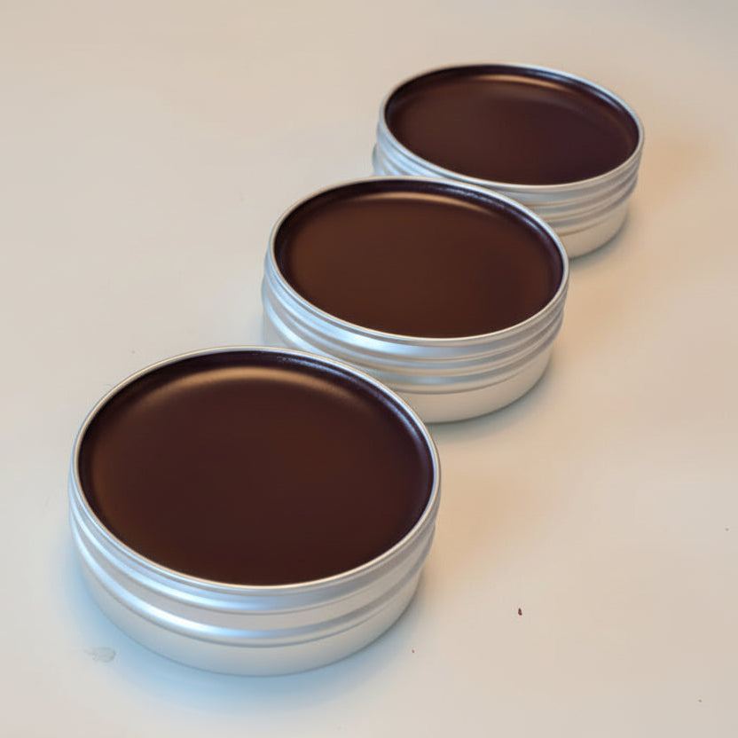 Three metal tins with dark chocolate-like lip tint tins on a white surface